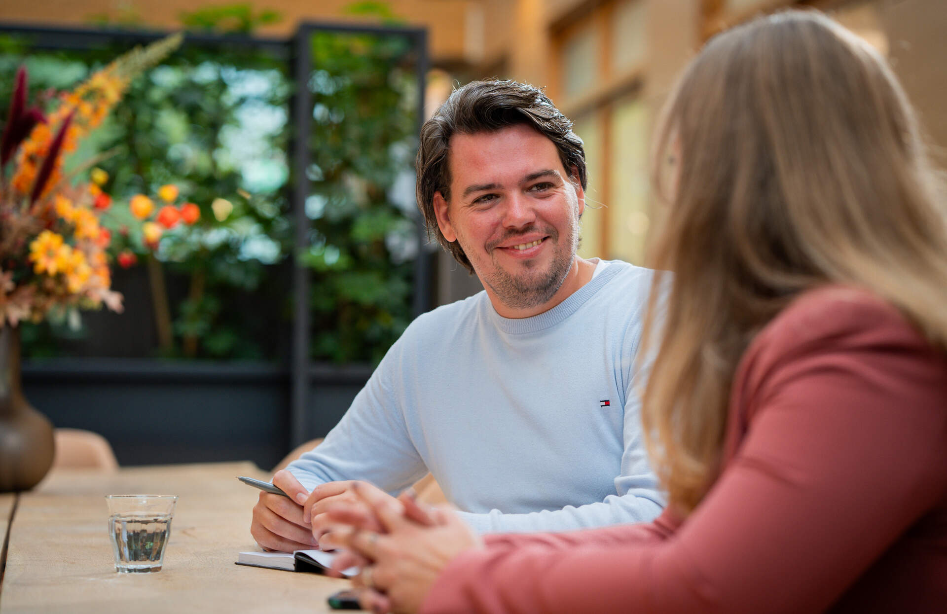 Collega lacht vriendelijk naar collega met wie hij in gesprek is.